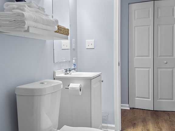Well-kept bathroom with a clean vanity sink, wall shelving for linens, and nearby closet storage for everyday essentials.