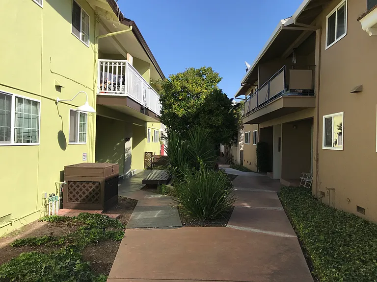 Cozy 600 square foot apartment with a front porch entry that opens to a landscaped common area and concrete walkway with wooden benches.