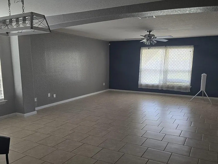 Spacious open living area with tile flooring, ceiling fan, and large windows with blinds for natural light and privacy.