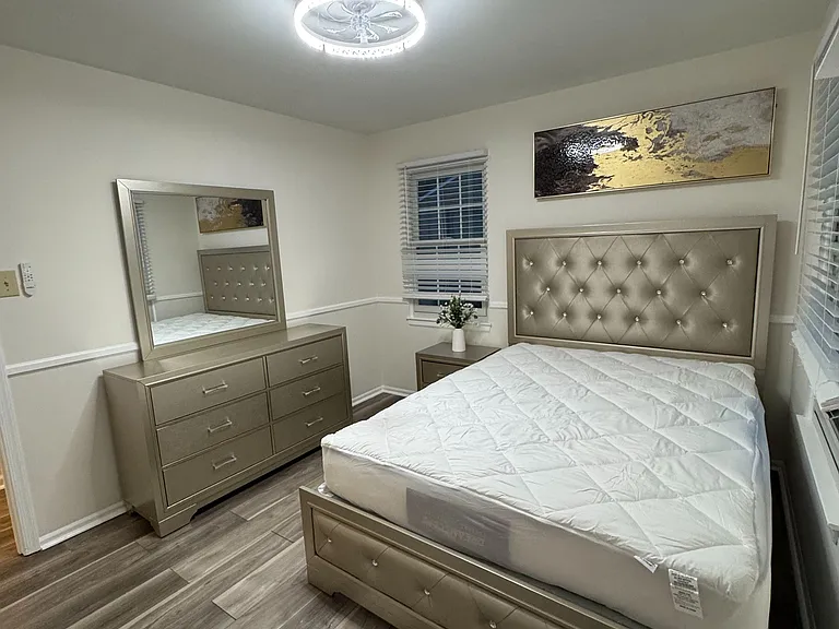 Furnished bedroom with a full bed, dresser with mirror, and wood-look flooring, plus windows with blinds for privacy.