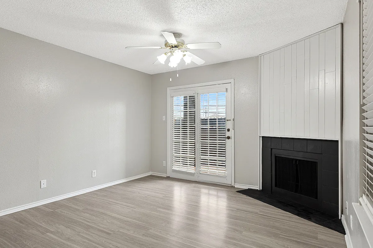 A bright living room is shown with vinyl floors, cozy fireplace, and view of private patio. - ReNew Holiday Hill