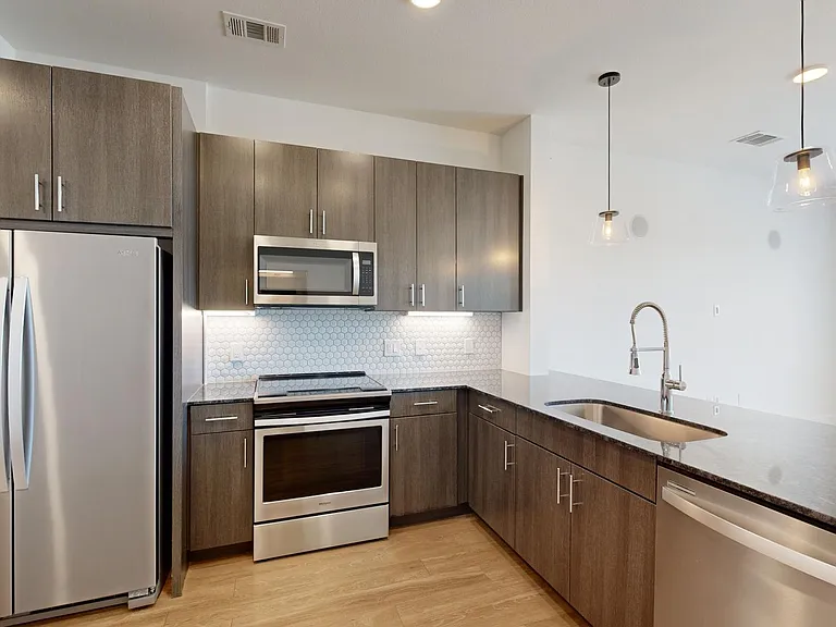 Apartment kitchen with stainless steel appliances, granite countertops, and wood-style flooring.