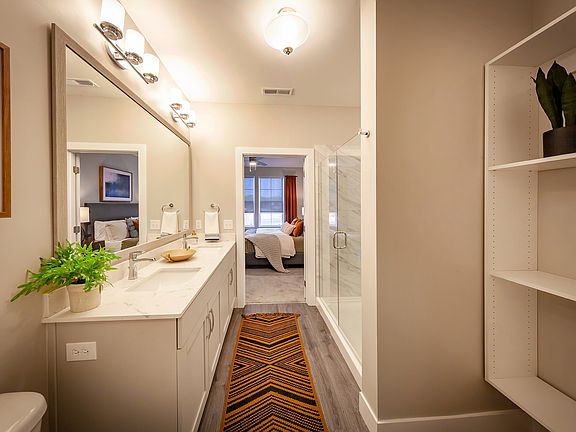Modern apartment bathroom featuring elegant fixtures, a spacious vanity, glass-enclosed shower, and direct access to a private bedroom suite.