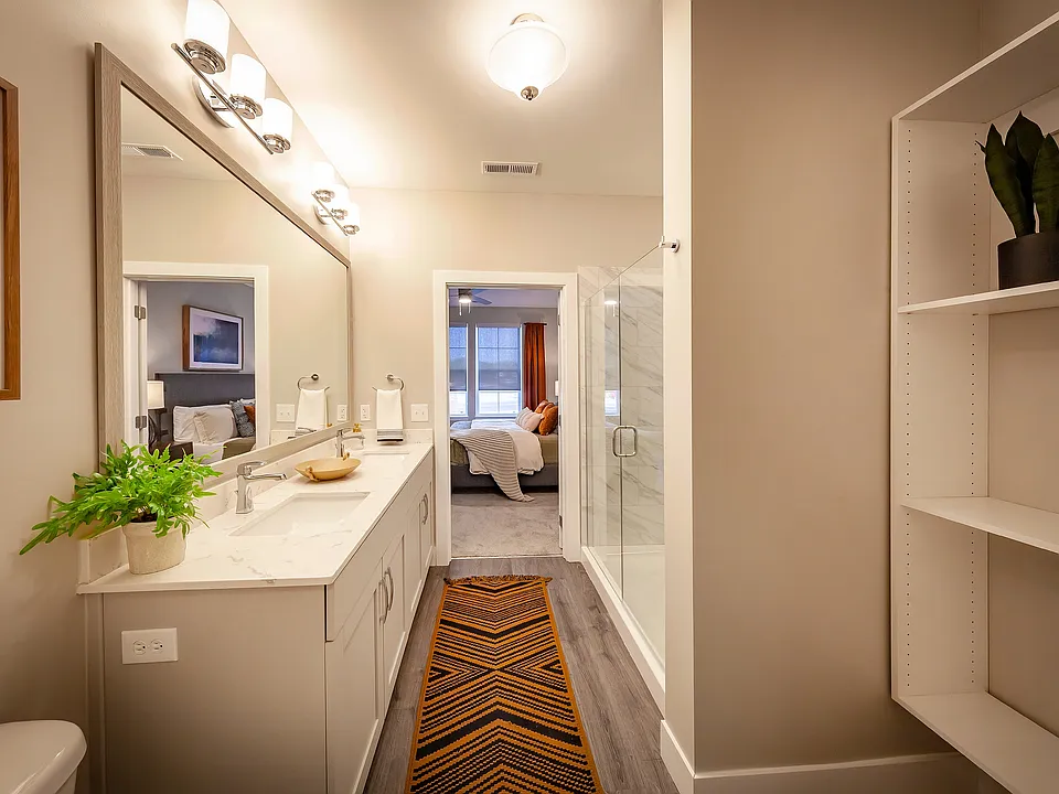 Modern apartment bathroom featuring elegant fixtures, a spacious vanity, glass-enclosed shower, and direct access to a private bedroom suite.