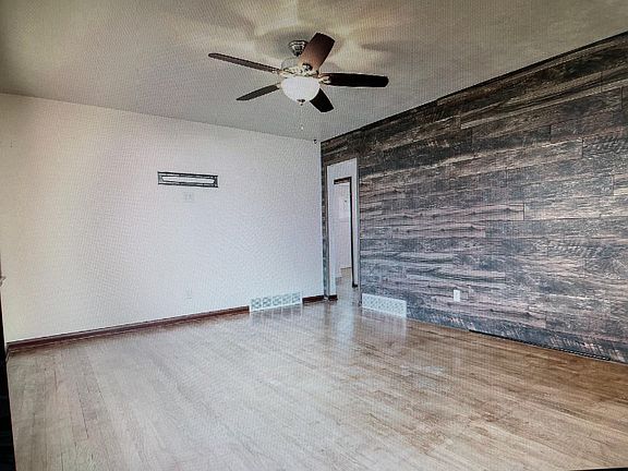 Spacious living room showing a wood accent wall. Ceiling fan and tv bracket too!