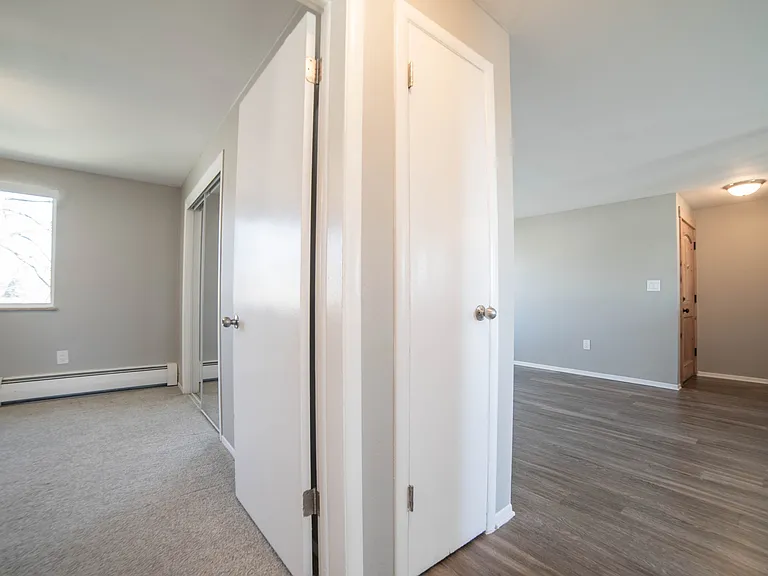 Modern apartment hallway featuring elegant wooden flooring, bright natural light, and doors leading to spacious rooms.