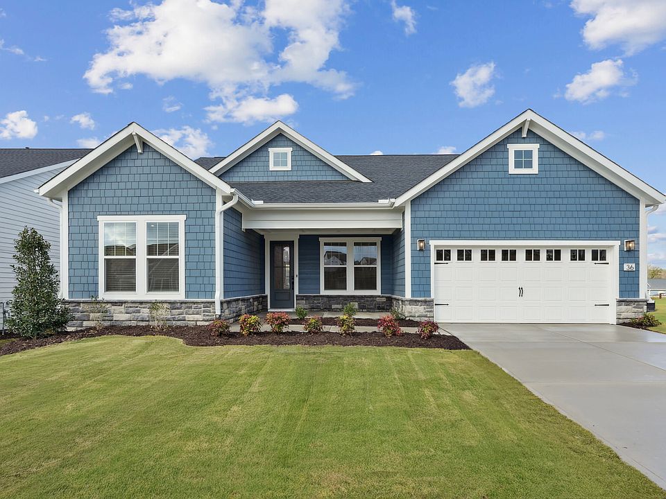 A well-manicured lawn surrounds a two-story house with a gray exterior, a white garage door, and a c