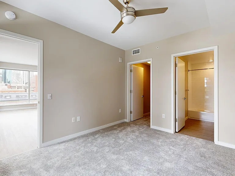 Spacious apartment bedroom with large closet, attached bathroom, and plush carpet flooring.