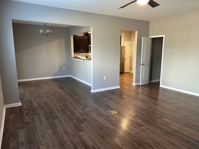 A view from the far corner of the living room, where on the left is the dining area that has an exterior door to the patio, to the far right (out of view) is the hall toward the front door, the open door on the right is the half bath, and the far lit area