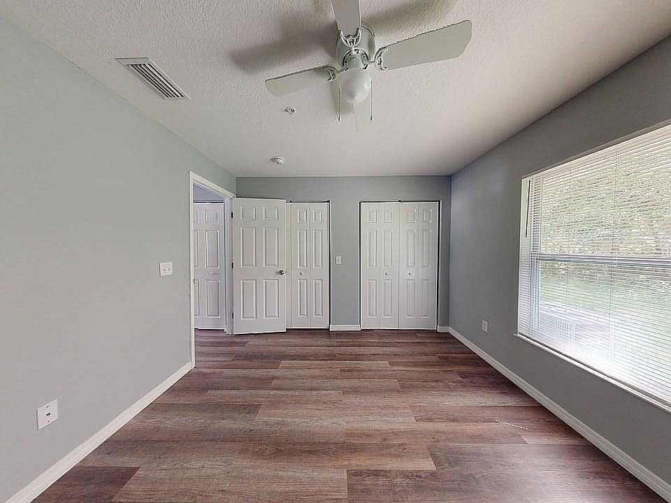 Bright and airy bedroom with modern gray walls, elegant wooden flooring, and ample closet space, enhanced by a large sunlit window.