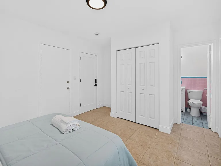 Spacious bedroom with tile flooring, double-door closet storage, and convenient access to a nearby bathroom.