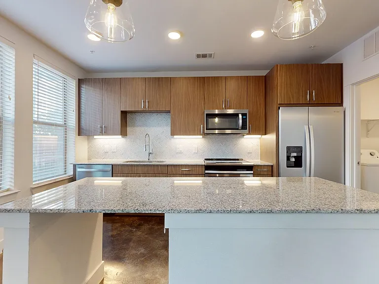 Apartment kitchen with stainless steel appliances, granite countertops, and polished concrete flooring.