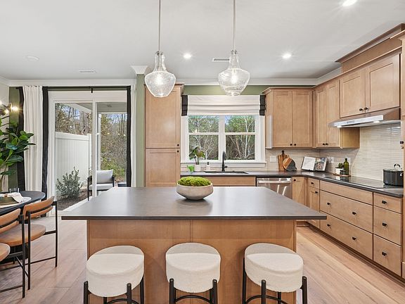 A modern and spacious kitchen with wooden cabinets, a large island with stools, and pendant lights i