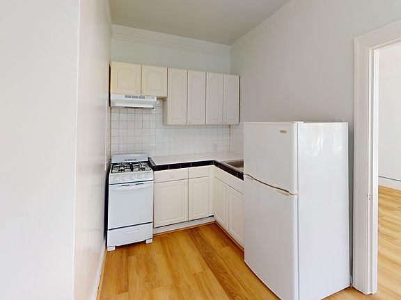 Kitchen with multiple cabinets, refrigerator, stove, range hood, and sink
