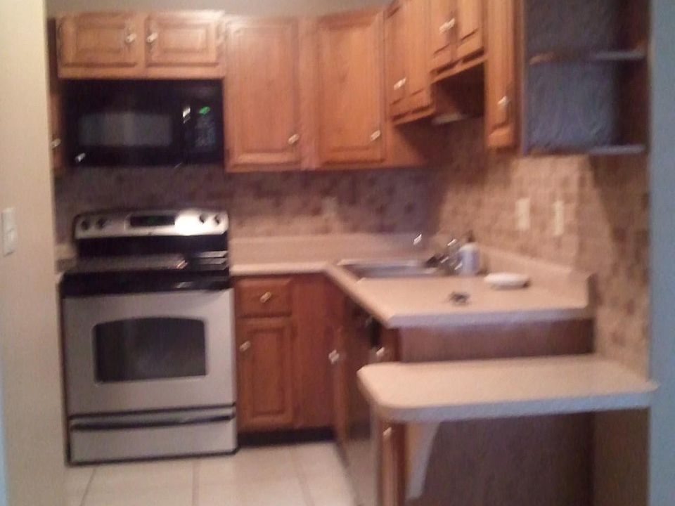 Kitchen with stainless steel appliances and tiled backsplash. View from laundry closet/second bath area.