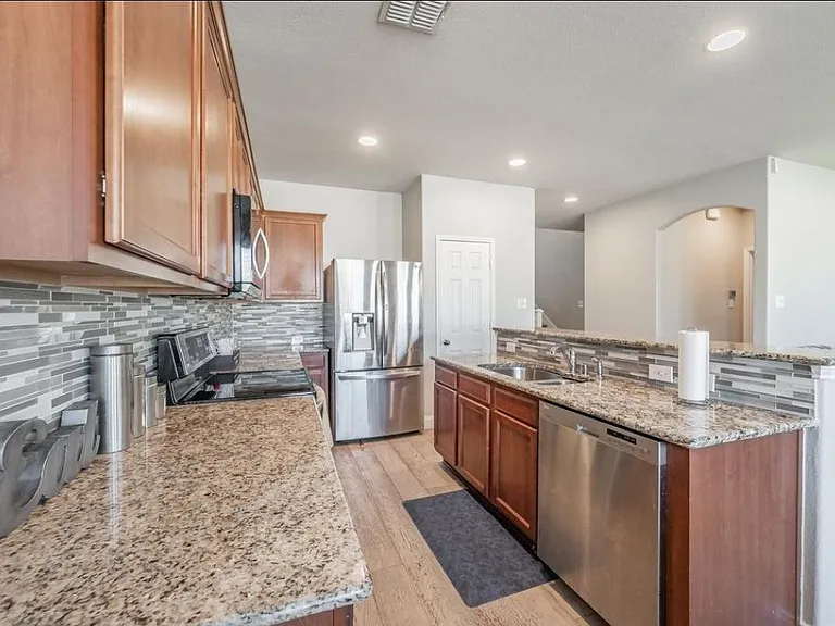 Open-concept kitchen with granite counters, mosaic tile backsplash, and stainless steel appliances plus a large breakfast bar