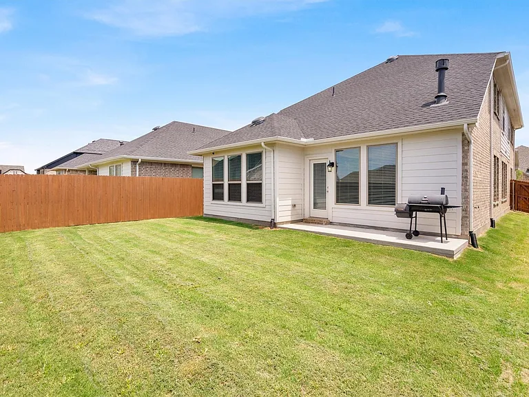 Expansive backyard featuring a manicured lawn, a full wood privacy fence, a concrete patio, a white paneled exterior, and a dark shingle roof