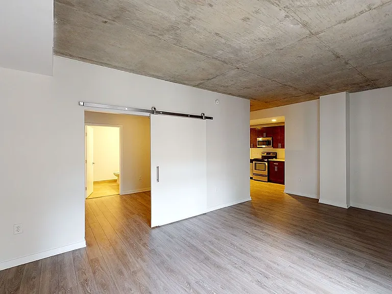 Apartment kitchen with stainless steel appliances, dining and living room with wood-style flooring.