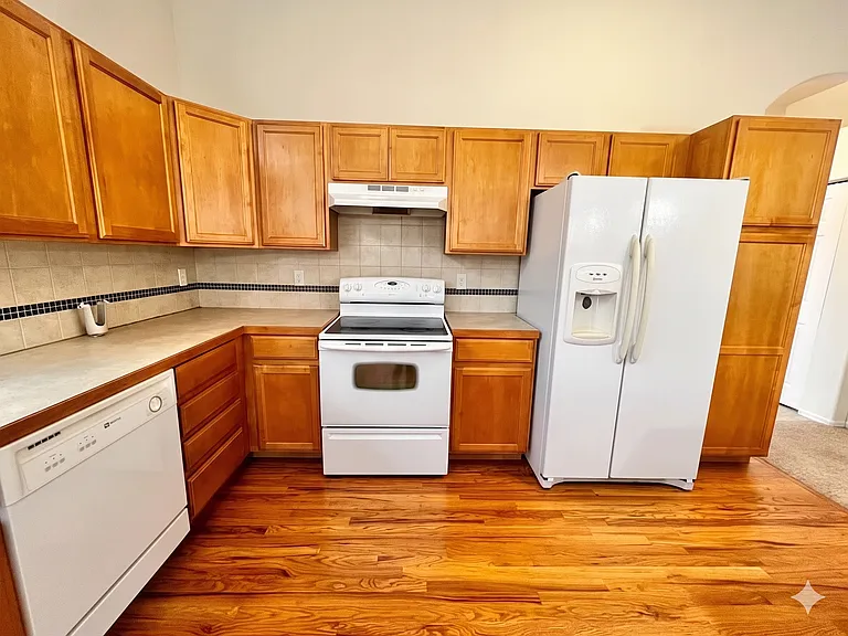 View of kitchen: sinks and dishwasher to the left, oven and range (center), and refrigerator and pantry space (right).