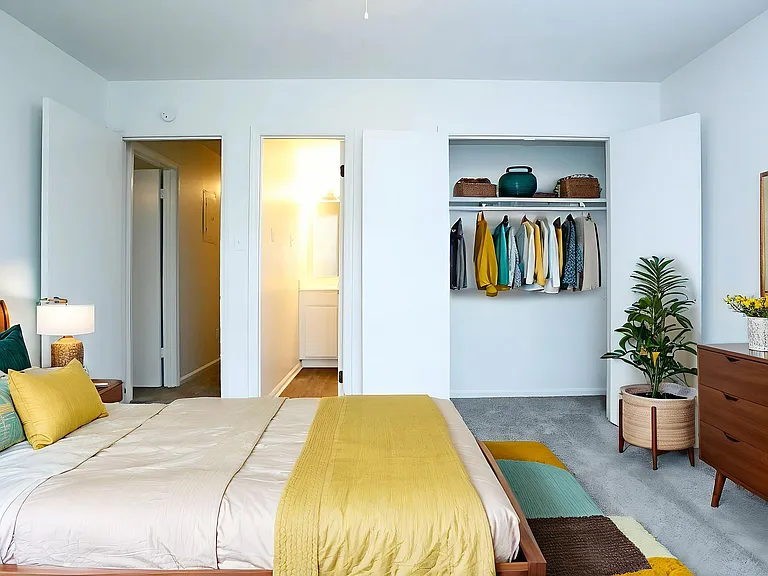 Inviting bedroom with elegant decor, featuring a cozy bed with vibrant pillows, a modern open closet with colorful attire, and stylish furniture accented with fresh greenery.
