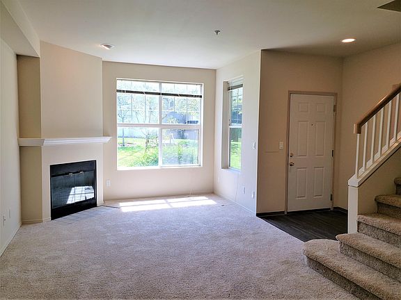 Living room with wood burning fireplace, entry, and stairs to the second floor.
