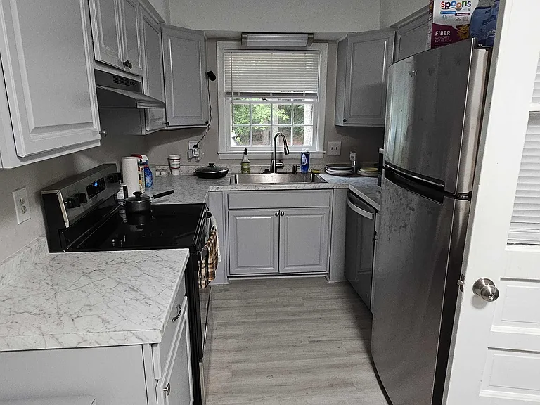 Galley kitchen with ample cabinetry, stone-look counters, stainless refrigerator, and a sink set beneath a window.