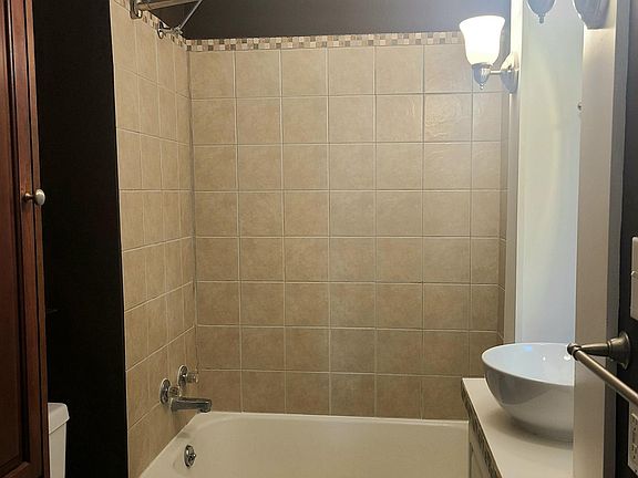 Fully tiled tub surround with tile floor; large cabinet to the left for toiletries etc.