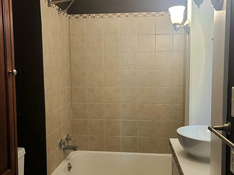 Fully tiled tub surround with tile floor; large cabinet to the left for toiletries etc.