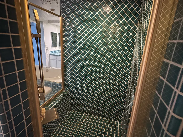 Enclosed green-tiled, stand-up shower with regular shower head and knee-level faucet for washing feet or filing buckets.