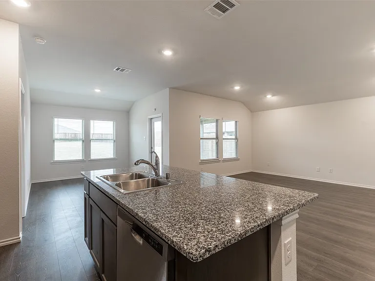 Kitchen island featuring a double basin stainless steel sink, a chrome faucet, and a dishwasher, with granite countertops