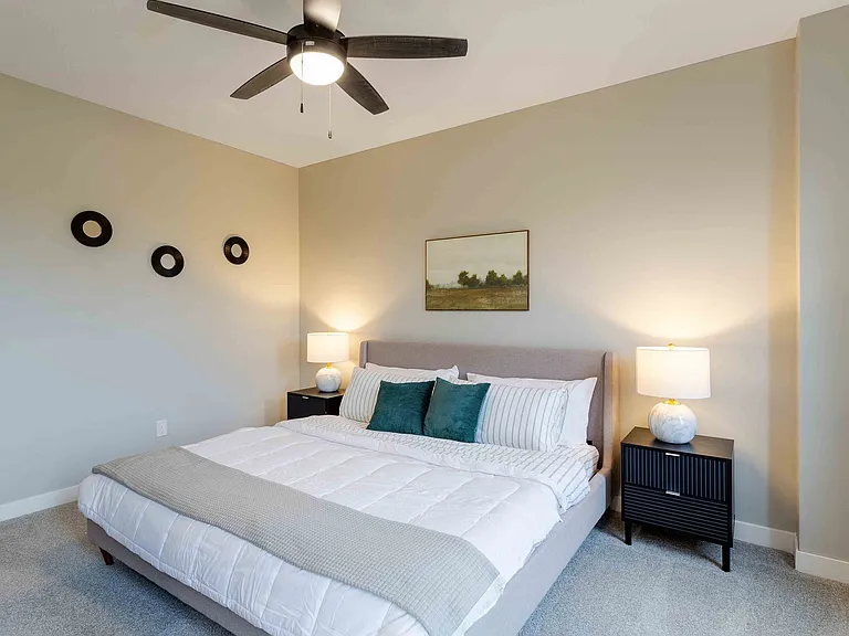 Cozy bedroom featuring a plush king-sized bed with elegant linens, stylish nightstands, and ambient lighting under a modern ceiling fan.