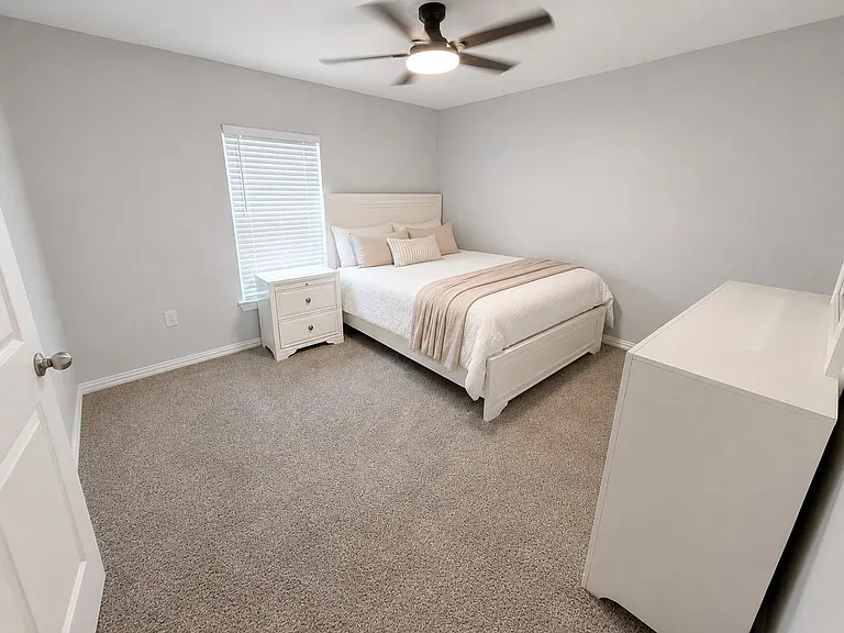 Well-sized bedroom with a ceiling fan, plush carpeting, and a window with blinds, plus dresser and nightstand storage.