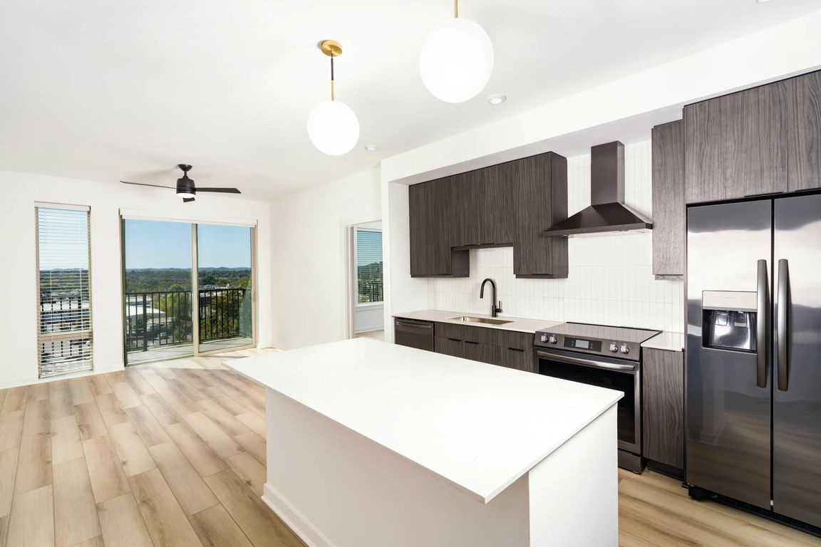 An open kitchen at Modera Nations in Nashville features a spacious island and the choice of light or dark finishes, with skyline views extending the living space.