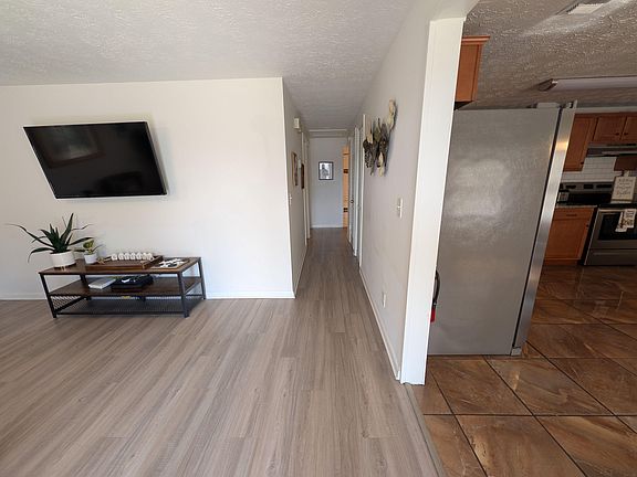 Open common area with durable wood-look flooring, wall-mounted TV, and easy access to the adjacent kitchen.