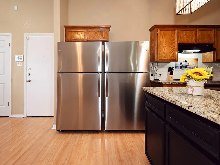 Kitchen features stainless steel double-door refrigerator, ample cabinetry, and a granite island for extra prep space.