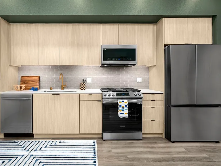 Finish Package I Kitchen with light oak cabinetry, white quartz countertop, grey tile backsplash, and stainless steel appliances