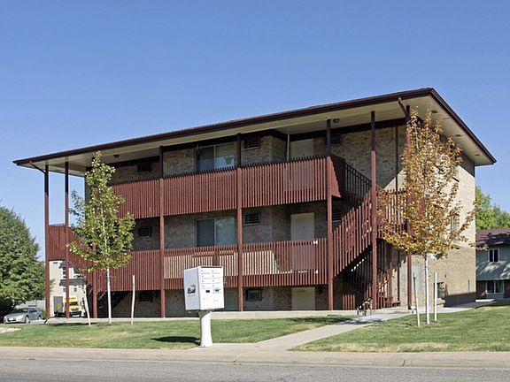 Charming three-story apartment building with brick exterior and wooden accents, nestled in a lush green environment.