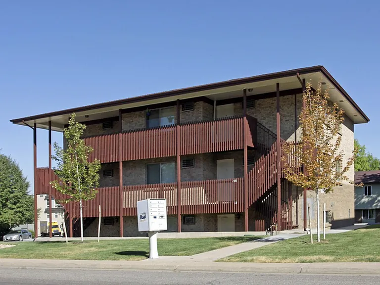 Charming three-story apartment building with brick exterior and wooden accents, nestled in a lush green environment.