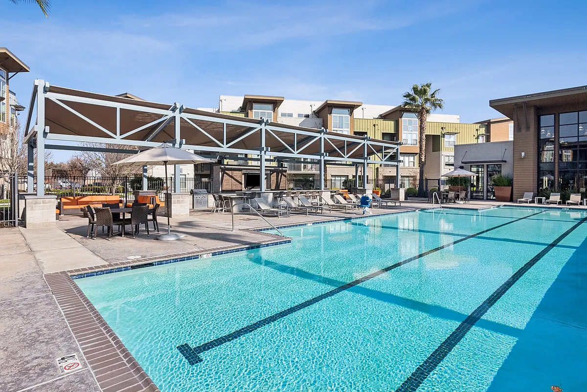 Aspire Apartments Tracy California Luxury Living A large swimming pool in front of a building with palm trees. - Aspire Apartments