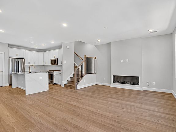 A spacious and modern open-concept living space with a kitchen, staircase, and a fireplace, featurin