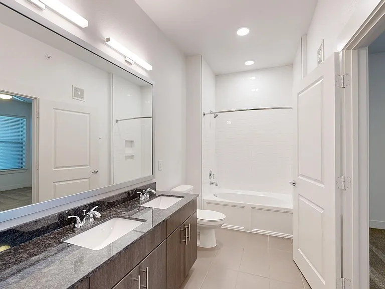 Apartment bathroom with large soaking tub, tile flooring, and double sinks.