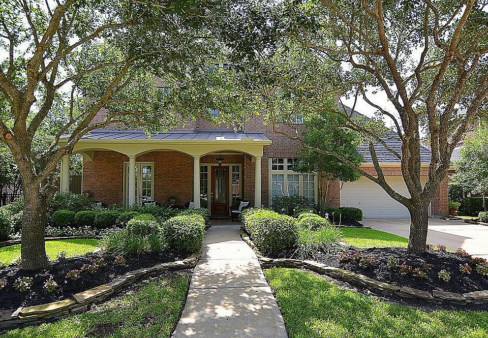 Front of property with large covered porch, mature lush landscaping on a cul-de-sac street.