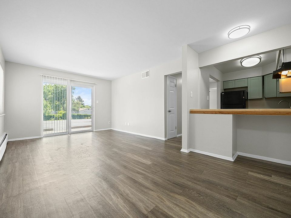 Bright and spacious living room with sleek hardwood floors, natural light through glass doors, and a modern open-concept kitchen with stylish cabinetry.