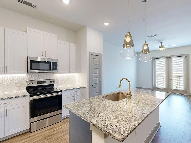 Apartment Kitchen with Stainless Steel Appliances, Dining and Living Room with Wood Style Flooring.