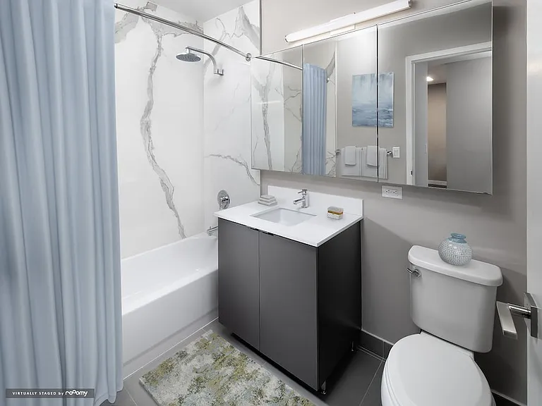 Renovated Package II bath with grey cabinetry, white quartz countertop, and marble-style porcelain tub surround