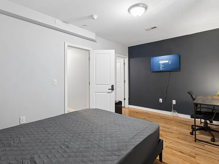 Spacious bedroom with hardwood floors, a mounted TV, and a dedicated desk workspace plus secure keypad entry.