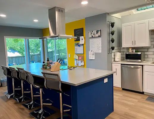 Remodeled kitchen with a 10' island featuring ample storage, soft-close drawers, trash/recycle pull-out bins, and outlets with USB ports at both ends. A true hood vent adds style and function, while double sliding doors fill the space with natural light.