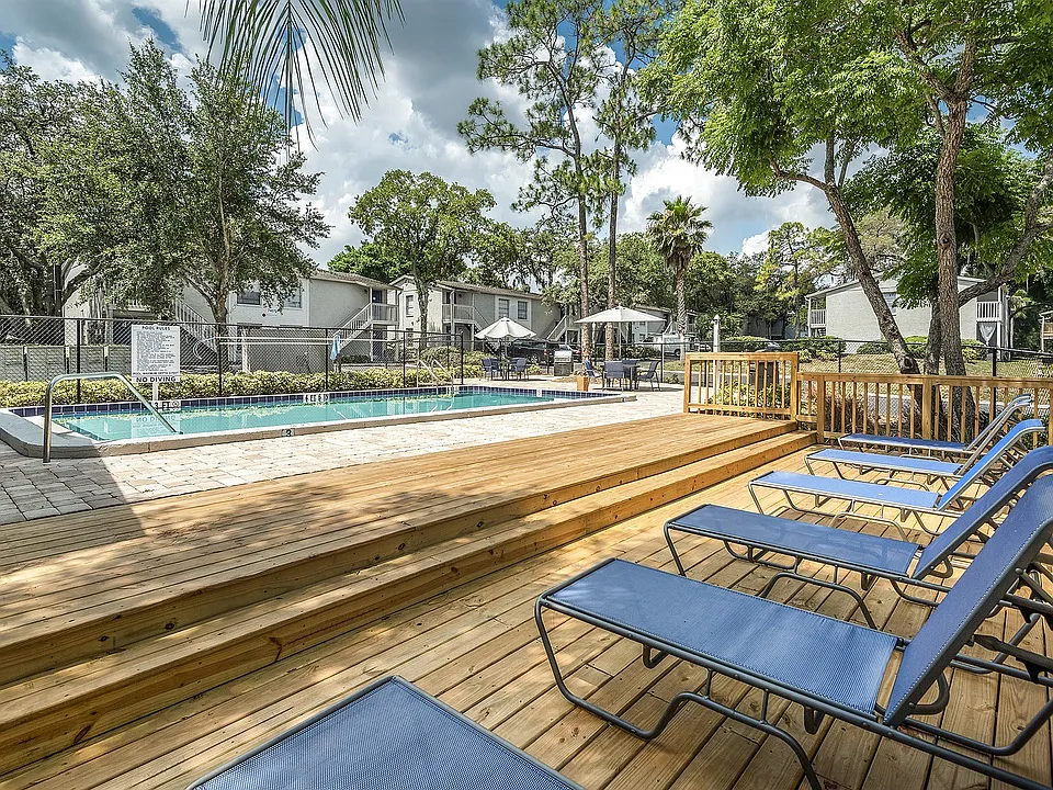 Inviting outdoor pool area with sun loungers, surrounded by lush greenery and contemporary apartment buildings, perfect for relaxation.