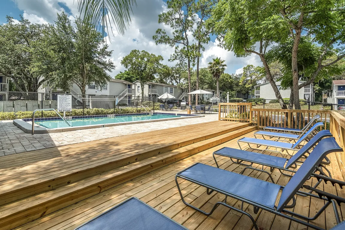 Inviting outdoor pool area with sun loungers, surrounded by lush greenery and contemporary apartment buildings, perfect for relaxation.