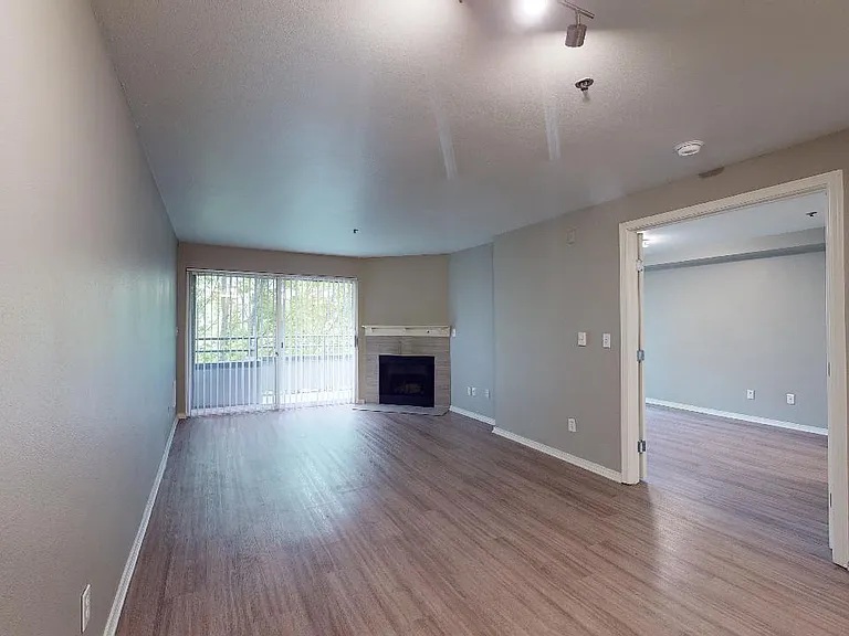 Apartment living room with wood-style flooring, fireplace and balcony in select homes.